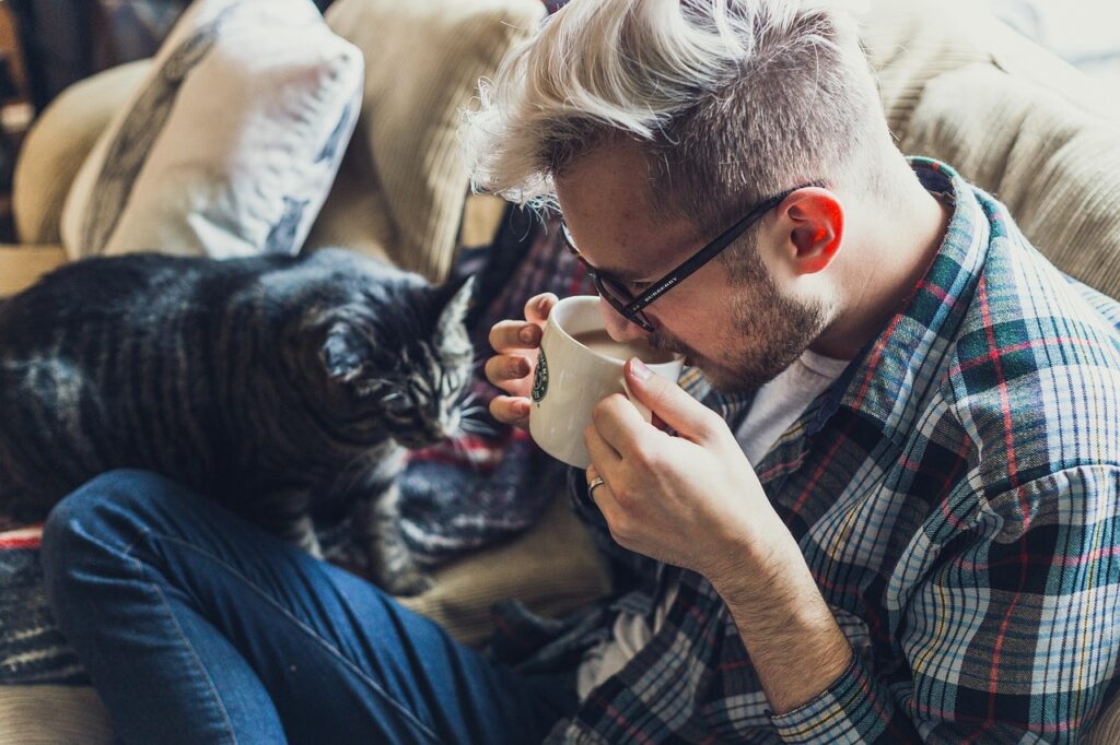 man, sofa, coffee, coffee cup, mug, animal, cup, drink, drinking coffee, morning coffee, coffee break, caffeine, drinking, adult, cat, pet, couch, indoors, leisure, portrait, seat, sitting